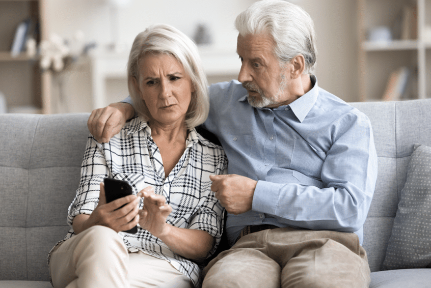 Image of an elderly couple sitting on a couch looking at a cell phone